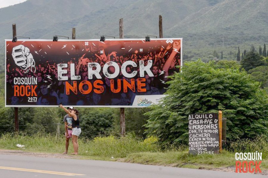 FOTO FACEBOOK COSQUIN ROCK LA PREVIA. Una pareja se saca una selfie frente a un cartel con el anuncio del Festival, en la Ruta cerca de Santa Mar&iacute;a Punilla.