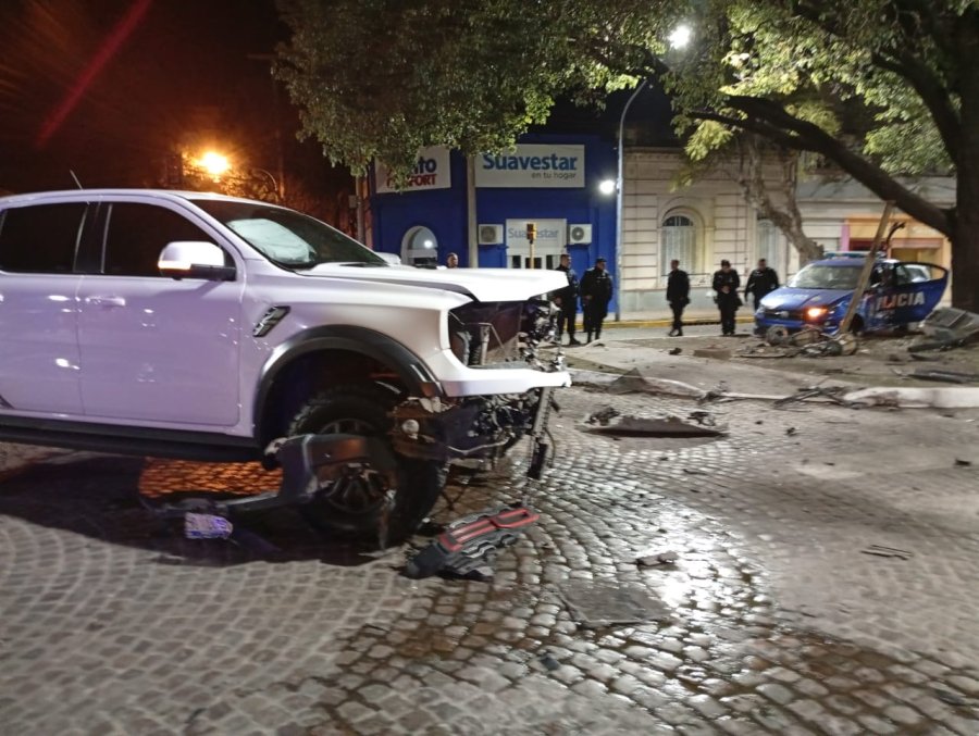 La camioneta Ford Raptor con la trompa destruida, más atrás el patrullero Fiat contra un árbol tras arrancar el semáforo peatonal.