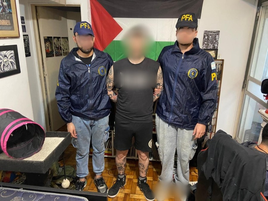 El hombre de 37 a&ntilde;os detenido junto a dos agentes de la Polic&iacute;a Federal, detr&aacute;s una bandera de Palestina. (FOTO PRENSA POLIC&Iacute;A FEDERAL)