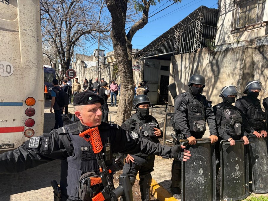 En primer plano, un cord&oacute;n de efectivos de seguridad, m&aacute;s atr&aacute;s detenidos rumbo a los m&oacute;viles mientras observan el ministro Cococcioni y el intendente Viotti entre otros.